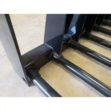 Detail of black painted tubular steel tines welded to a reinforced support frame on concrete floor indoors