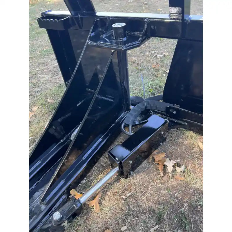 Close-up of black steel tractor attachment with hydraulic cylinder and angled mounting bracket on grass with dry leaves