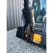 Black concrete mixer attachment mounted on loader arm with visible hydraulic connection over gravel surface