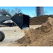 Black skid steer loader bucket attachment dumping loose dirt or mulch in outdoor worksite environment