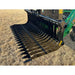Black metal grapple attachment with evenly spaced curved tines mounted on green tractor loader arm over dry grass field