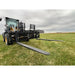 Loader attachment with extended black steel pallet forks and perforated backrest on grassy field under overcast sky