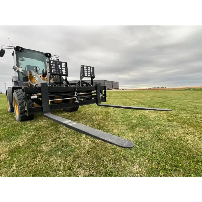 Loader attachment with extended black steel pallet forks and perforated backrest on grassy field under overcast sky