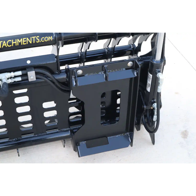 Black steel skid steer grapple attachment with mounting bracket, hydraulic hoses, and reinforced connection points on concrete surface