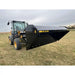 Black hydraulic dump bucket attachment mounted on front of compact tractor on grassy field with overcast sky