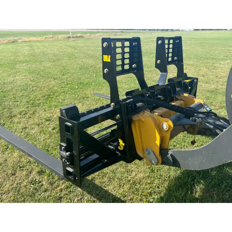 Black steel pallet fork attachment with perforated backrest mounted on yellow skid steer arm on grass field