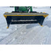 Black and yellow compact snow pusher attachment mounted on green skid steer loader arm over snow-covered ground