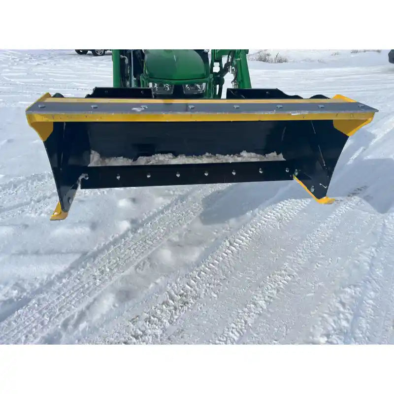 Black and yellow compact snow pusher attachment mounted on green skid steer loader arm over snow-covered ground
