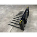 Angled left view of black steel manure spear attachment with ten pointed tines on concrete floor indoors