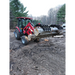 Red compact tractor with enclosed cab lifting multiple large logs using black grapple attachment on dirt ground outdoors