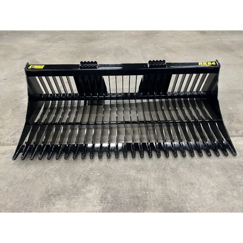 Front view of black metal skid steer rock bucket attachment with narrow spaced tines and reinforced top edge on concrete floor
