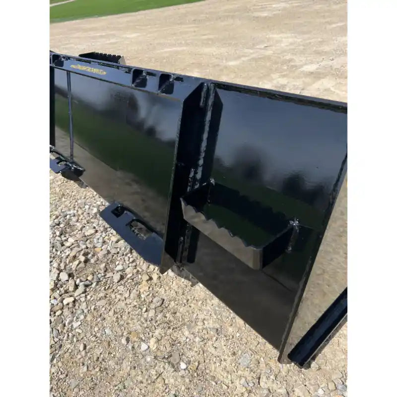 Rear view of black steel skid steer material bucket with step attachment and reinforced welds on gravel surface