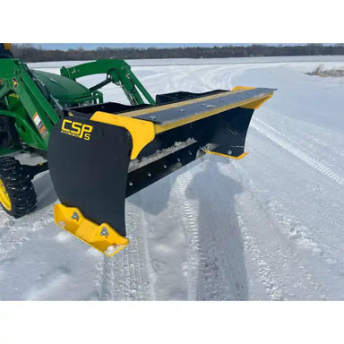 Yellow and black steel snow pusher attachment mounted on green compact loader clearing snow on open snowy terrain