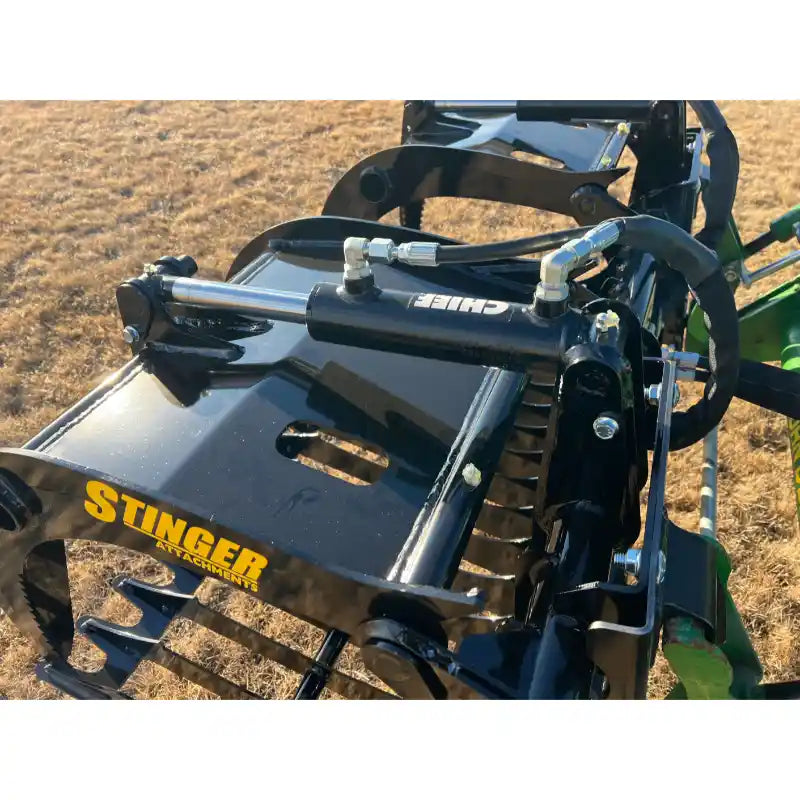 Close-up of black hydraulic rock grapple attachment with curved tines and reinforced frame on green tractor arm