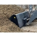 Close-up of black skid steer attachment scooping loose organic mulch at outdoor material storage site