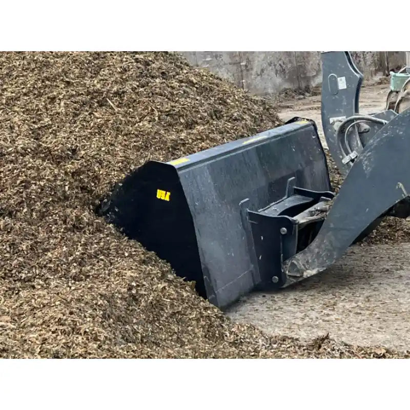 Close-up of black skid steer attachment scooping loose organic mulch at outdoor material storage site