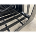 Close-up of black metal skid steer root grapple attachment with spaced curved tines and reinforced crossbars on concrete floor