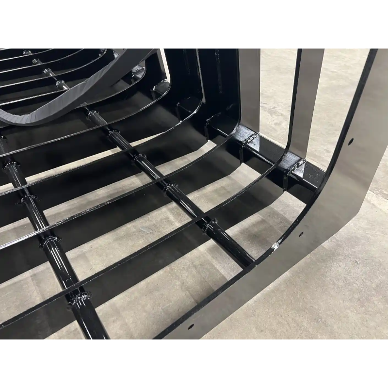 Close-up of black metal skid steer root grapple attachment with spaced curved tines and reinforced crossbars on concrete floor