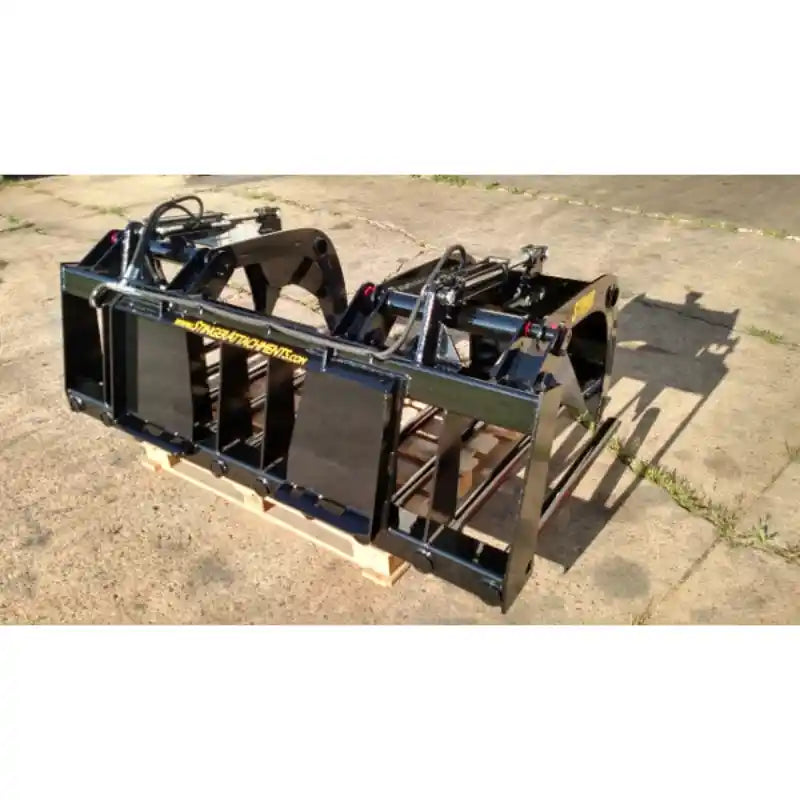 Black painted steel manure grapple attachment with dual hydraulic cylinders and spaced tine frame on pallet outdoors