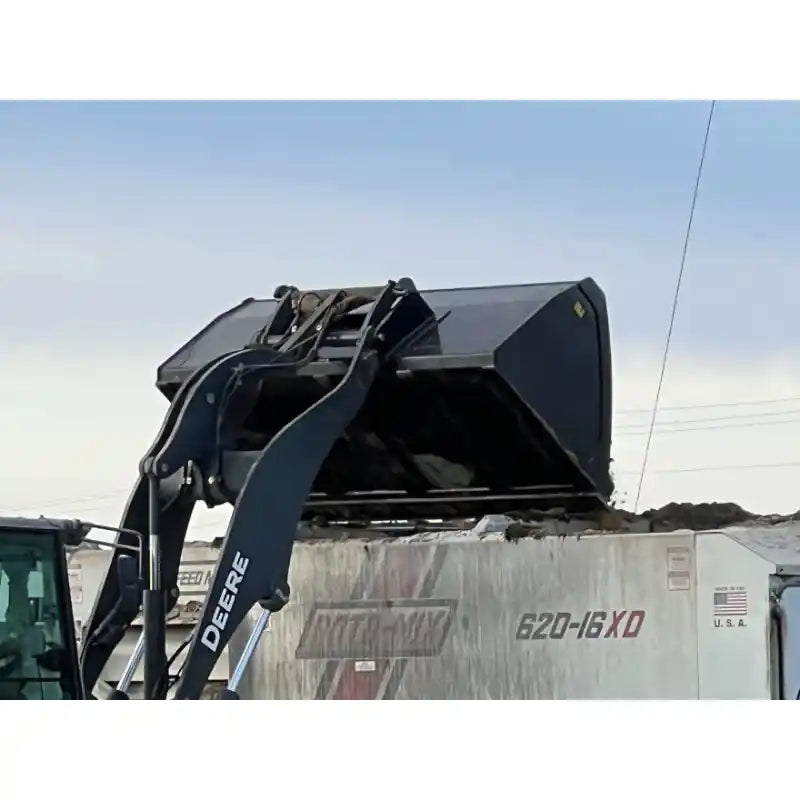 Close-up of black skid steer high-volume bucket attachment lifting loose soil above a dump truck outdoors