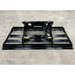 Front view of black steel skid steer land plane attachment with mounting frame and hydraulic hose on concrete floor