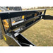 Close-up of black steel hydraulic dump bucket tipping plate attachment with hydraulic hose on grassy field