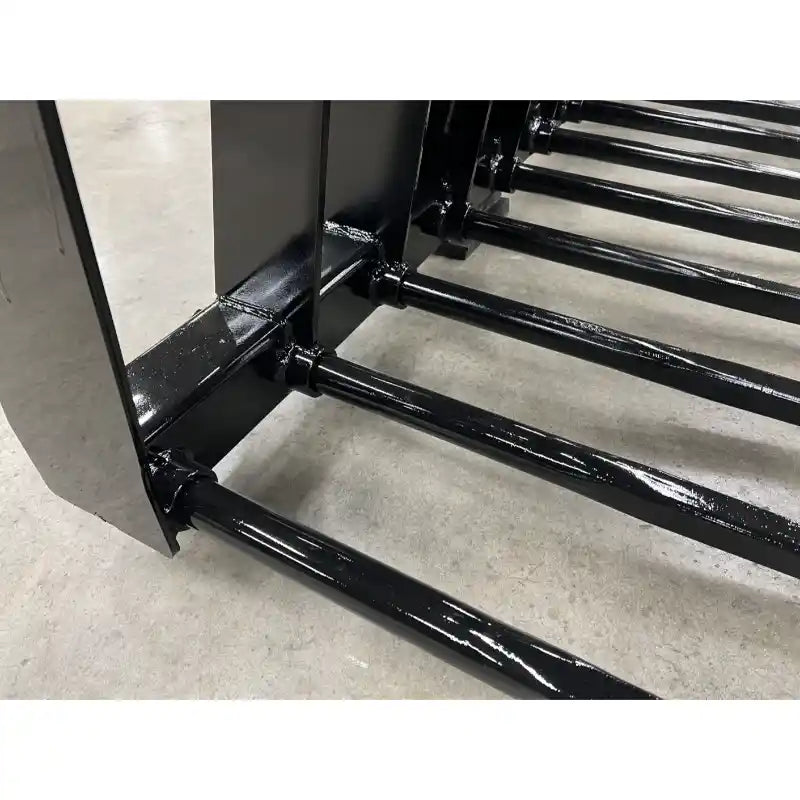 Close-up of black metal grapple tines with rounded spear tips and weld joints on concrete floor indoors