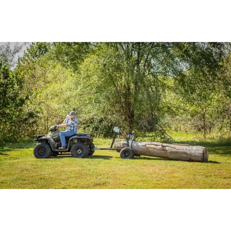 Man on ATV towing Swisher log skidder moving large log across grassy field, gallery position 1