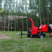 Side view of red MechMaxx 7-inch hydraulic feed wood chipper operating and ejecting wood chips, gallery position 1