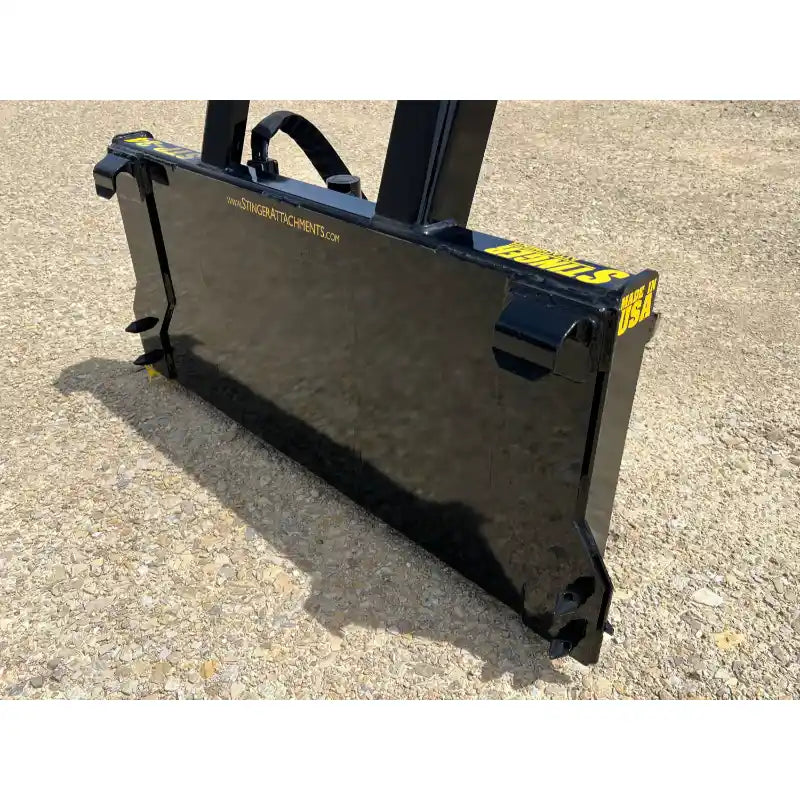 Black steel tractor-mounted tree puller attachment with smooth flat plate and reinforced mounting brackets on gravel surface