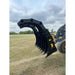 Black multi-tine clam-style grapple attachment mounted on loader arm with hydraulic hoses visible over grassy field