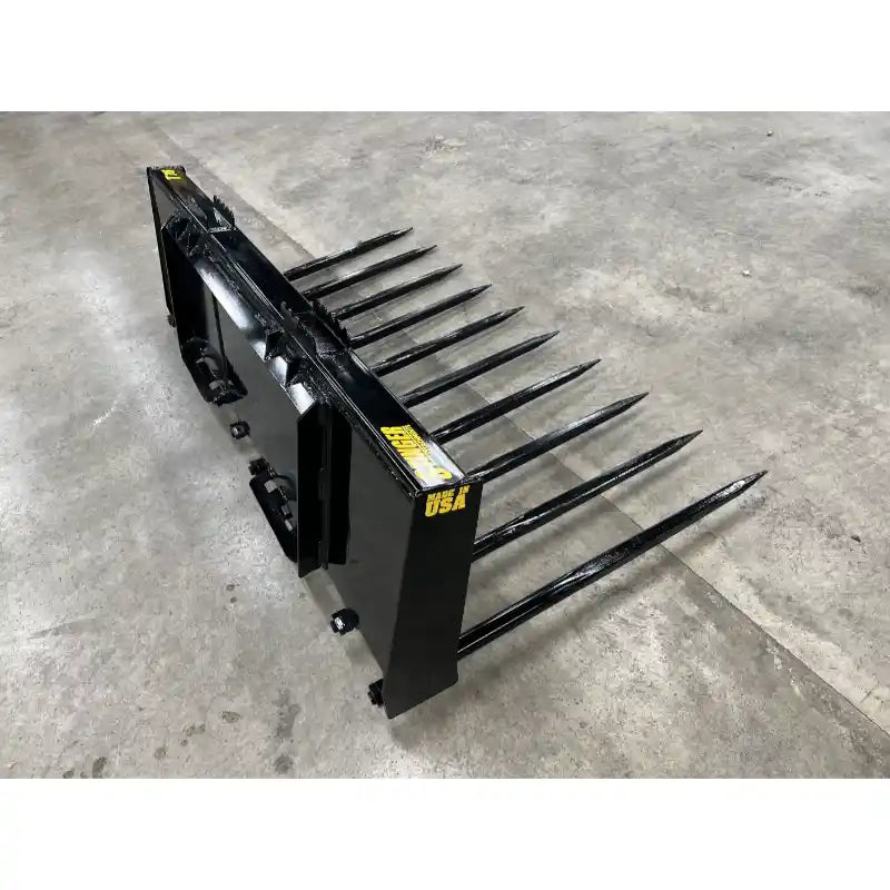 Black steel manure spear attachment with ten long tines and mounting bracket on concrete floor indoors