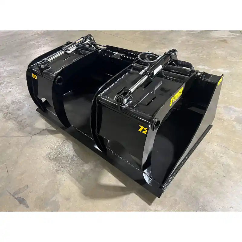 Black steel demolition grapple bucket with twin hydraulic cylinders and wide clamp arms on concrete floor indoors