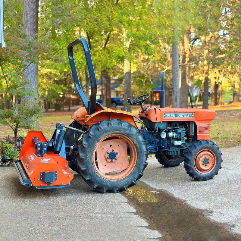 Side view of orange PTO driven flail mower attached to tractor with roll bar, positioned outdoors on concrete, gallery 1
