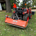 Rear angle of orange Ingersoll PTO flail mower attached to compact tractor, positioned on grassy area, gallery position 1