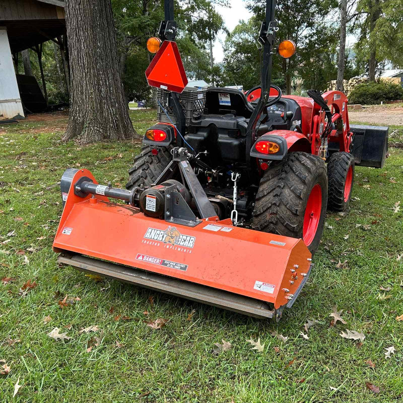 Rear angle of orange Ingersoll PTO flail mower attached to compact tractor, positioned on grassy area, gallery position 1