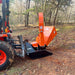 Orange PTO wood chipper mounted to tractor with vertical discharge chute, angled hopper, and black skid base