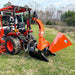 Orange PTO wood chipper attached to tractor with curved discharge chute, angled feed hopper, and black support frame