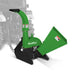 Green PTO wood chipper attachment with curved discharge chute, wide angled hopper, black frame, and tractor backdrop