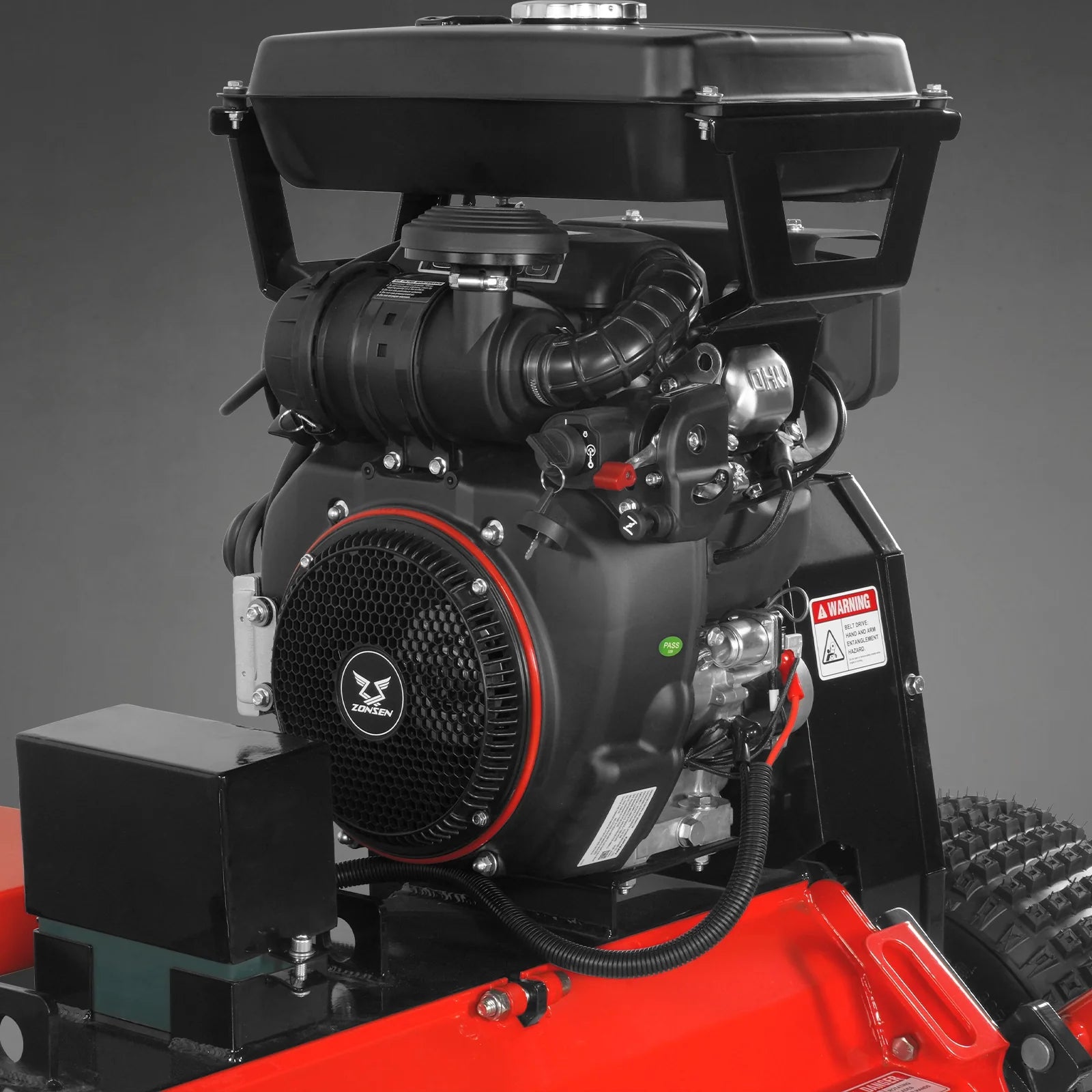 Black gasoline engine with recoil starter mounted on a red mower deck beside a treaded tire