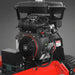 Black gasoline engine with recoil starter mounted on a red mower deck beside a treaded tire