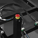 Black equipment frame with hydraulic hoses and a red push button on a yellow-labeled control post