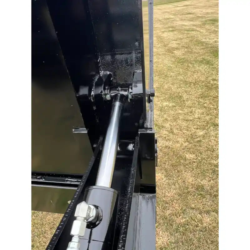 Close-up of hydraulic cylinder and hoses mounted inside black steel frame of tractor attachment over dry grass field