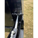 Close-up of hydraulic cylinder and hoses mounted inside black steel frame of tractor attachment over dry grass field