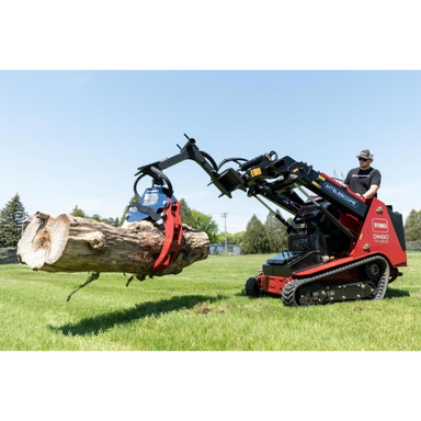 Mini skid steer with red and black hydraulic grapple lifting a large log on a grassy yard with operator wearing sunglasses and hat