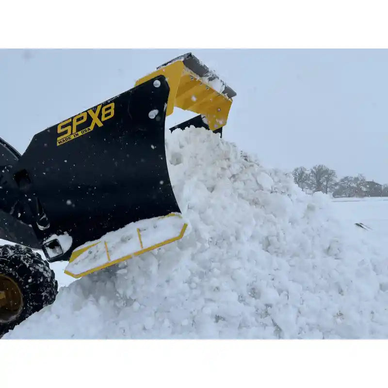 Black and yellow skid steer snow pusher attachment lifting and pushing a large mound of snow outdoors