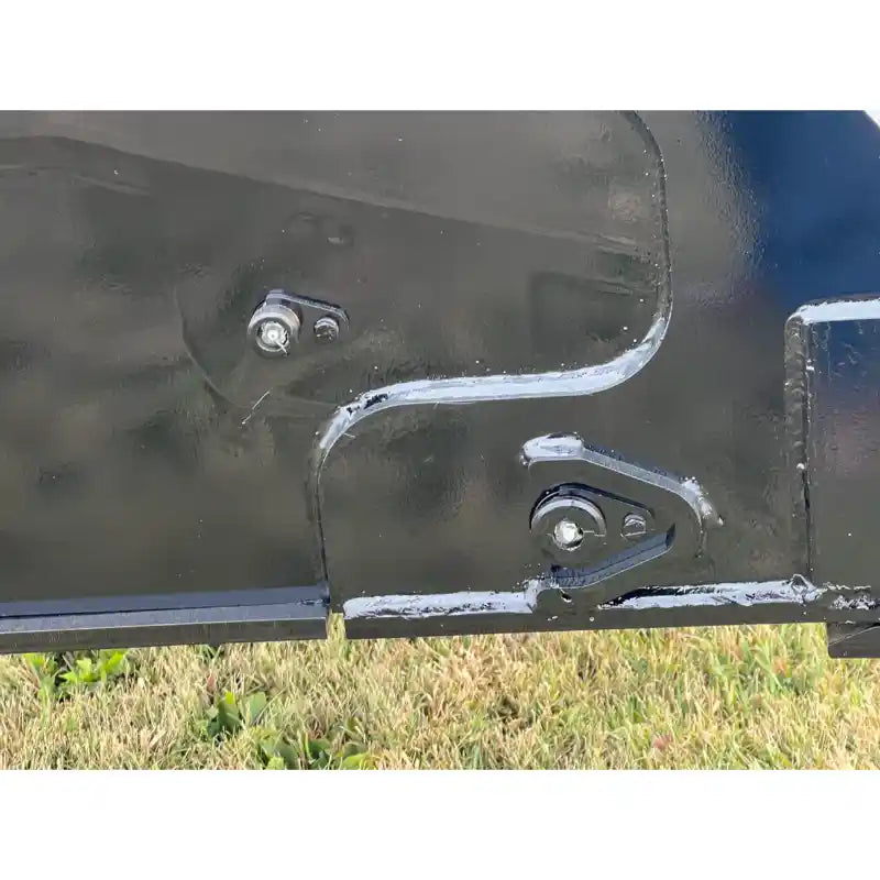 Close-up of black steel hinge components with bolts on hydraulic dump bucket attachment over grass