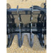 Close-up of black steel grapple attachment teeth with reinforced mounting brackets on gravel surface outdoors