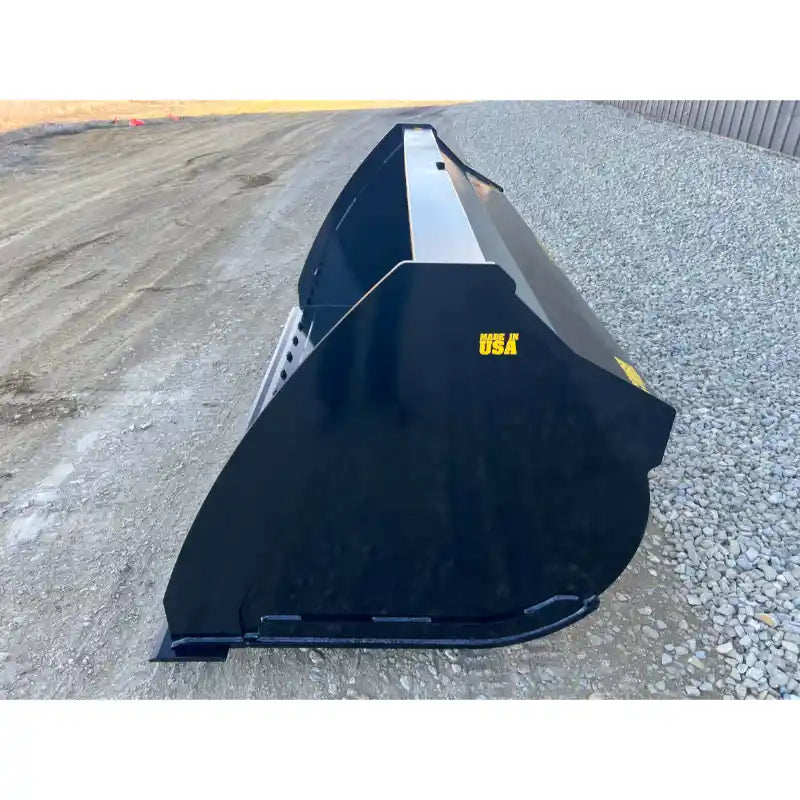Side view of a large black steel skid steer material bucket with smooth curved edges on gravel and dirt surface