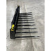 Black-painted steel manure spear attachment with ten long pointed tines and welded frame on concrete floor indoors